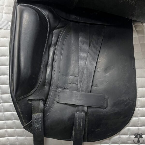 A black leather saddle bag sitting on top of a bed.