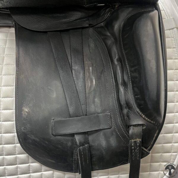 A black leather saddle bag sitting on top of a bed.