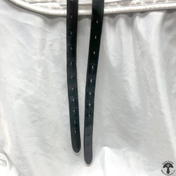 A pair of black leather straps hanging on the side of a white cloth.