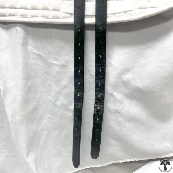 A pair of black straps hanging from the side of a white cloth.