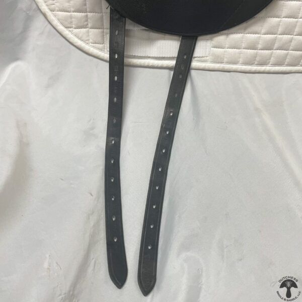 A pair of black leather straps hanging on the side of a white bag.