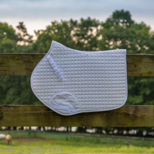 A white saddle pad hanging on the side of a fence.