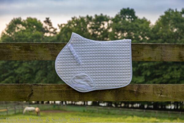 A white saddle pad hanging on the side of a fence.