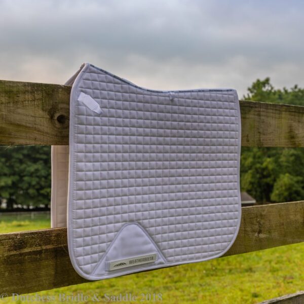 A white saddle pad hanging on the side of a fence.