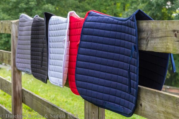 A row of horse saddle pads hanging on a fence.