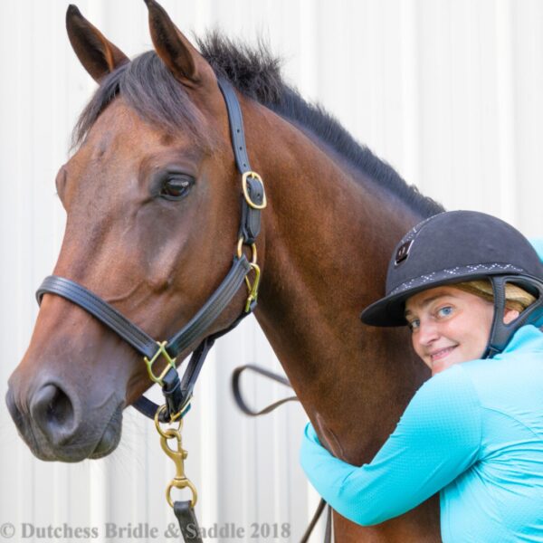 A woman in blue shirt holding on to the bridle of a horse.