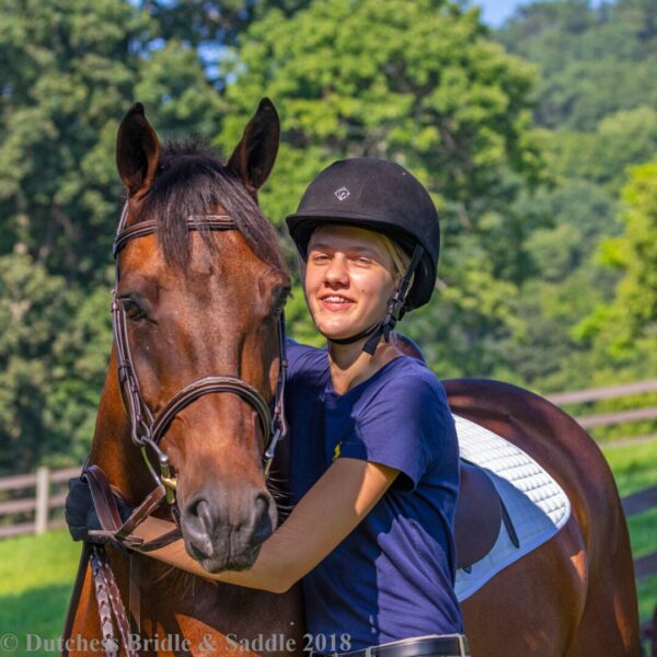 A woman in blue shirt holding on to brown horse.