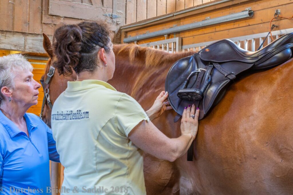 A woman is touching the saddle on a horse.