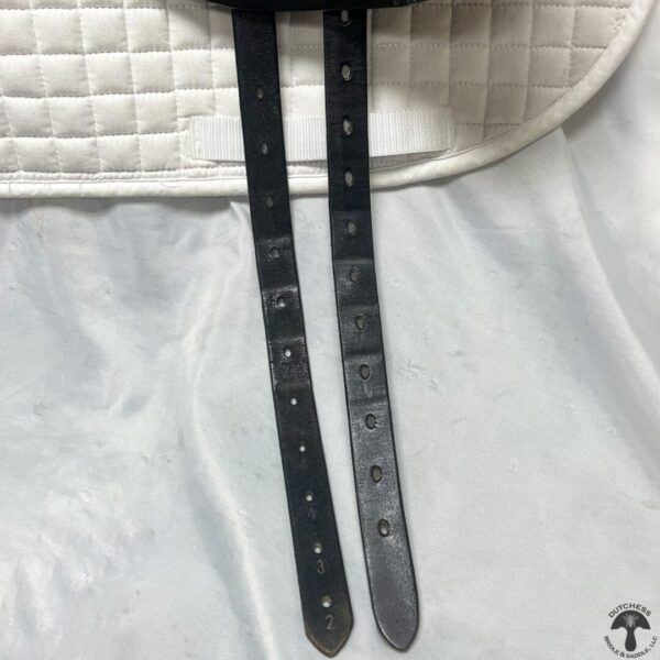 A pair of black leather straps hanging on the side of a white blanket.