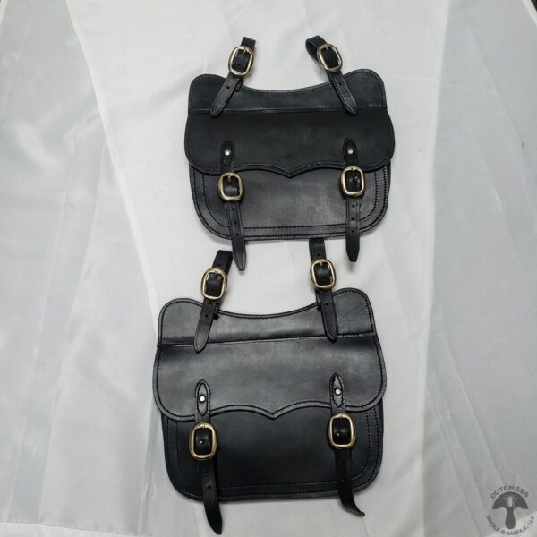 Two bags of black leather sitting on top of a white sheet.